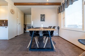 A dining area with a wooden table and chairs, a clock on the wall, and a window with blinds. - SanAlppi 7 by Holiday in Lapland (Levi)