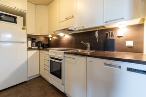Kompakti keittiö, jossa on valkoiset kaapit, sisäänrakennettu uuni, astianpesukone ja mikroaaltouuni.