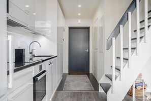 A modern kitchen with white cabinetry, a black countertop, and a grey door.