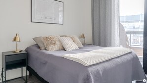 Ett modernt sovrum med en säng, två sänglampor, en inramad karta och utsikt över staden genom ett fönster.