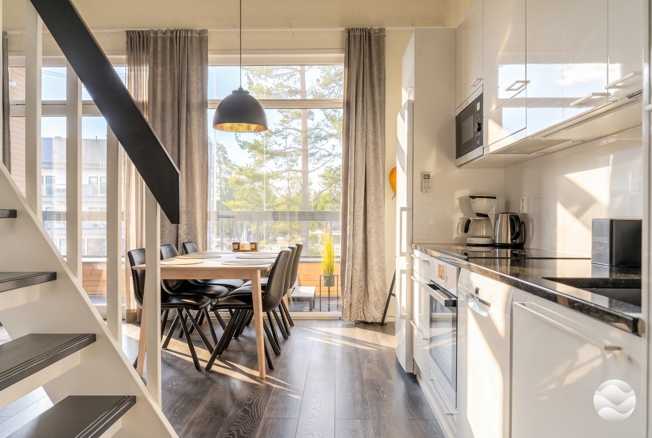 Een moderne keuken met witte kasten, een eethoek met een tafel en stoelen, en een trap naar een ander niveau.