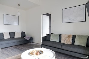 A modern living room with two grey sofas, a white coffee table, and framed maps on the walls.