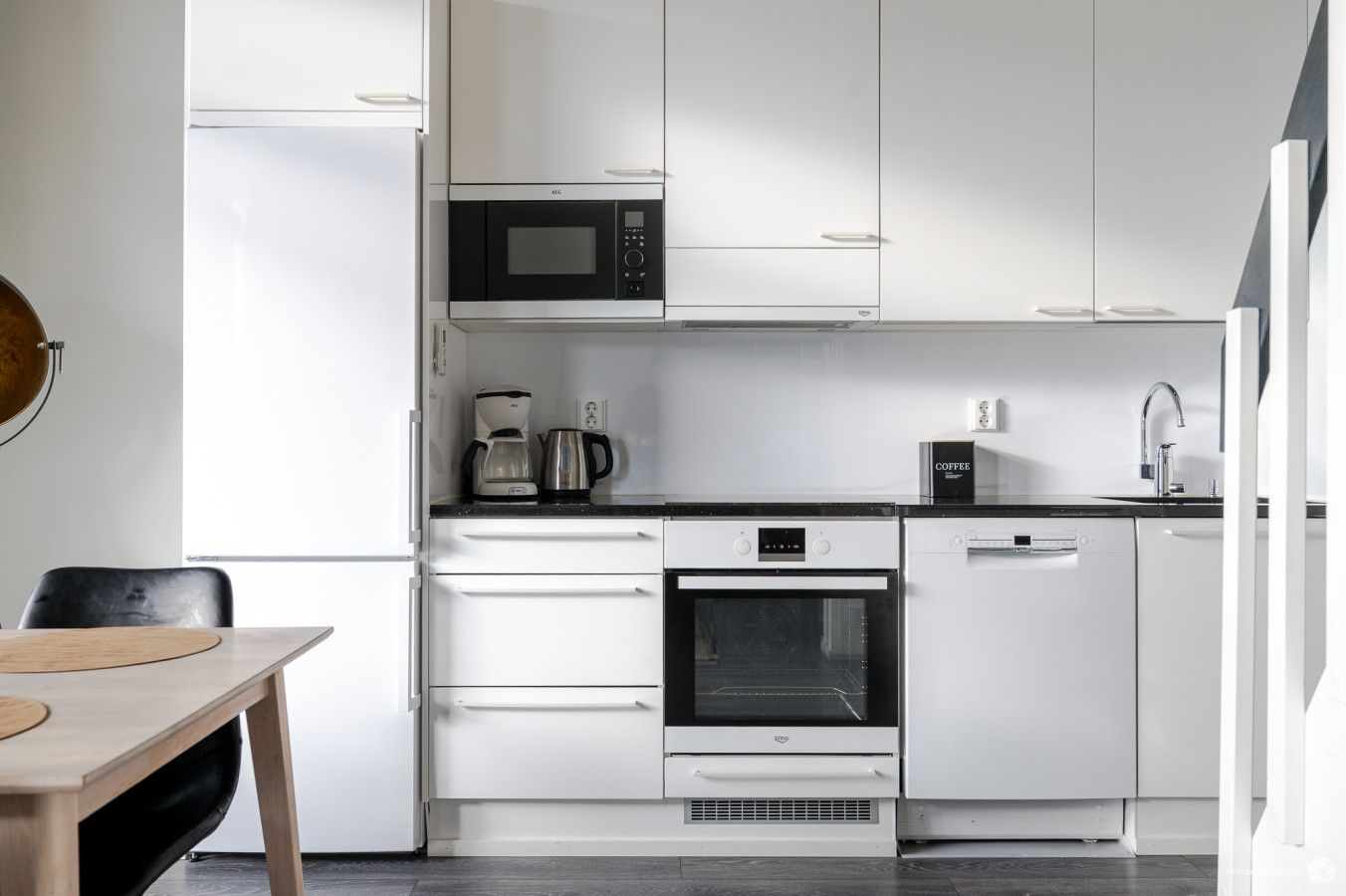 Une cuisine moderne dotée de meubles blancs, d’un four à micro-ondes, d’une machine à café, d’un four et d’un lave-vaisselle.
