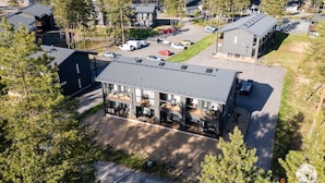 En moderne bygning med flere etager og fladt tag, omgivet af en parkeringsplads og tæt skov.