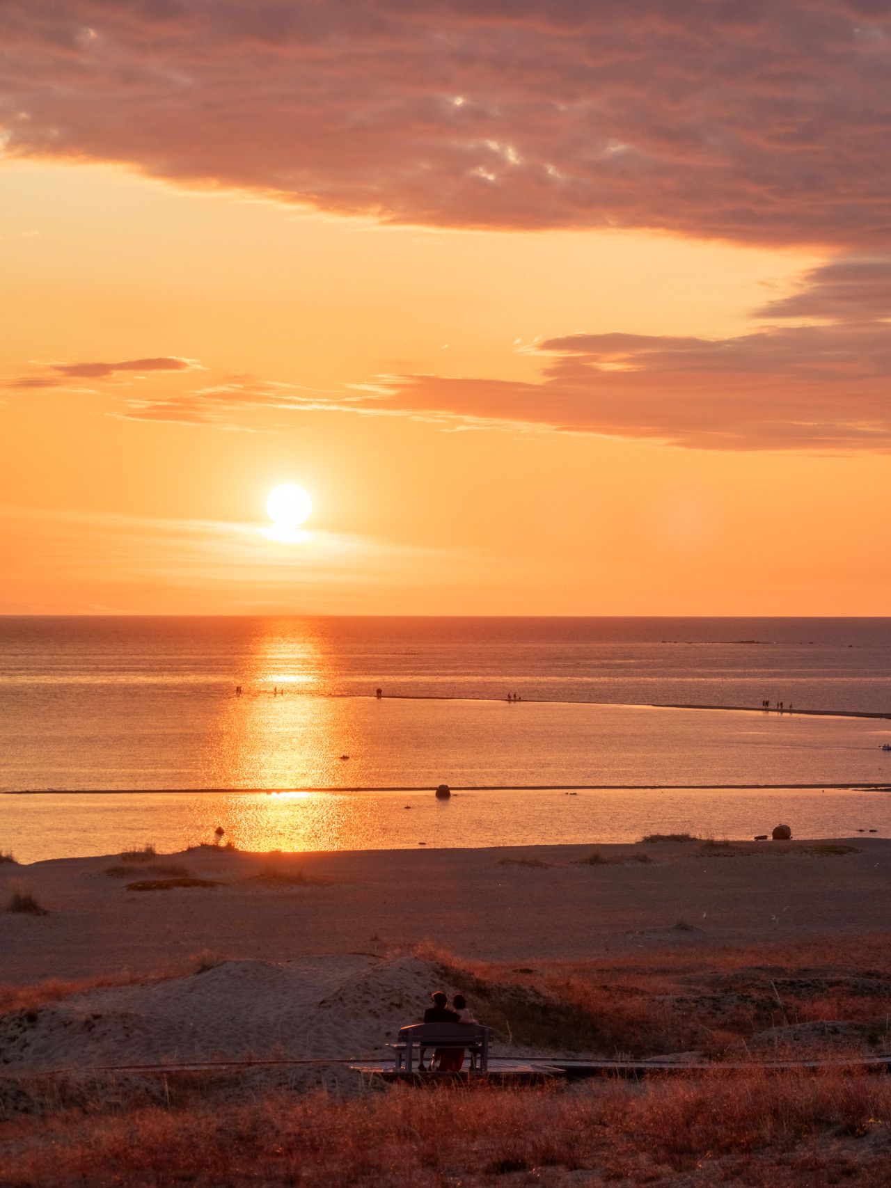 Un coucher de soleil sur une plage, avec une petite construction au premier plan.