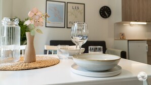 Et spisebord med en vase med blomster, et vinglas og en skål. Der er indrammede billeder på væggen og et ur.