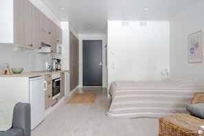 A compact bedroom with a bed, a small kitchenette, and a door leading to another room.