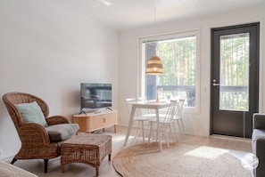 A living room with a dining table, chairs, a television, and a wicker sofa.