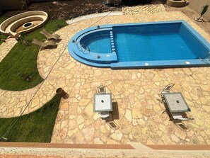 A swimming pool with a stone deck, two lounge chairs, and a circular garden feature. - Riad Jamilas - Room with Pool Access, Spa & Hammam near Ouarzazate (Ouarzazate)