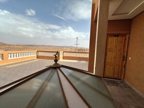 A room with a view of a desert landscape, a balcony with a railing, and a wooden door. - Riad Jamilas - Room with Pool Access, Spa & Hammam near Ouarzazate (Ouarzazate)