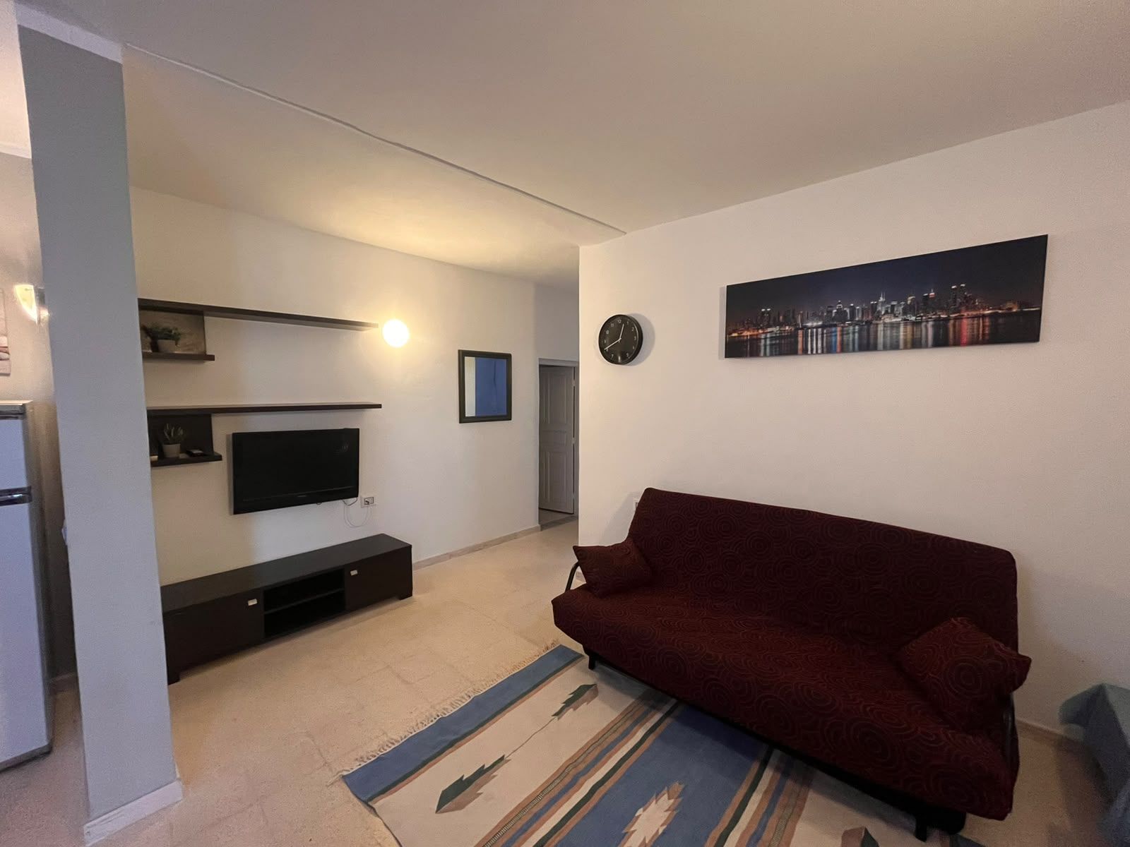 Un salon avec un canapé, un téléviseur et un tableau représentant un paysage urbain.