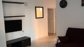 A living room with a flat-screen TV, a red sofa, a patterned rug, and a clock on the wall.
