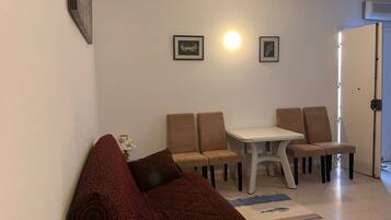 A living room with a sofa, a dining table with chairs, and a patterned rug.