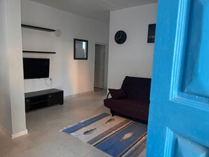 A living room with a flat-screen TV, a dark-colored sofa, a patterned rug, and a clock on the wall.