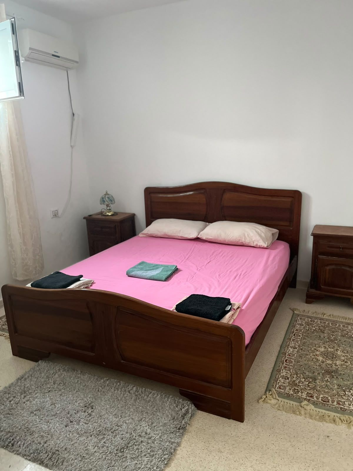 Une chambre avec un lit simple, une tête de lit en bois, une couvre-lit rose et un tapis gris.