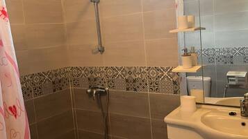 Une salle de bain avec une douche, un lavabo, un miroir et une fenêtre.