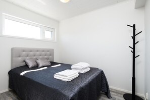 Ein Schlafzimmer mit einem Bett, Kissen, einem Nachttisch und einem schwarzen Kleiderständer.