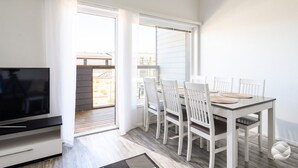 Ett modernt vardagsrum med en platt-TV, en matplats med bord och stolar samt en skjutdörr i glas som leder ut till ett utomhusområde.