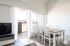 Ein modernes Wohnzimmer mit Flachbildfernseher, einem Essbereich mit Tisch und Stühlen sowie einer Glastür zum Außenbereich.