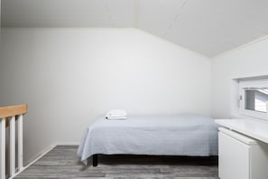A small, neatly arranged bedroom with a single bed, a window, and a white desk.