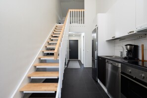 Une cuisine moderne dotée d’un four encastré et d’un escalier en bois menant à une mezzanine.