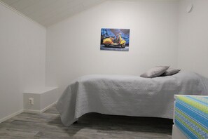A bedroom with a bed, a painting on the wall, and a small bedside table.