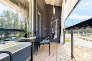 A modern outdoor balcony with a wooden floor, a black table, a chair, and a hanging hammock.