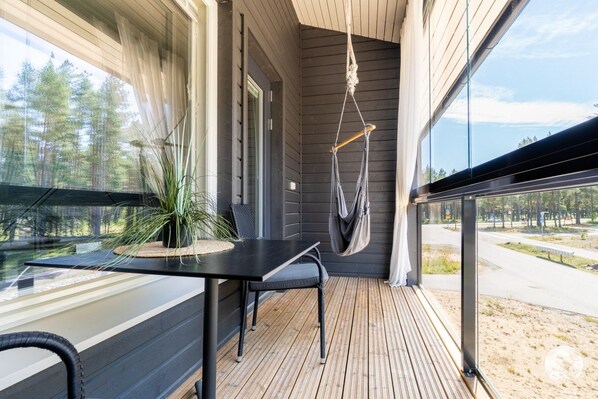 A modern outdoor balcony with a wooden floor, a black table, a chair, and a hanging hammock.