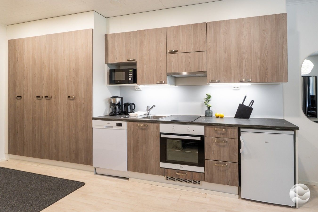 A modern kitchen with wooden cabinets, a built-in microwave, a coffee maker, and a refrigerator.