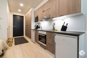 Cocina compacta con armarios de madera, microondas, cafetera y refrigerador pequeño.
