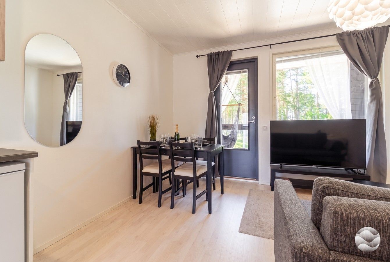 A living room with a flat-screen TV, a dining table with chairs, a sofa, and a large window with curtains.