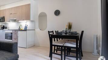 A modern kitchen with built-in appliances, a dining area with a table and chairs, and a wall-mounted clock.