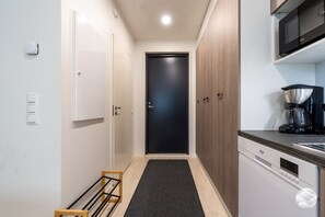 A narrow hallway with a dark door, white cabinets, a coffee maker, and a dishwasher.