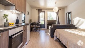 A modern kitchen with wooden cabinets, a dining area with a table and chairs, and a bedroom with a bed and a large window. - Meriheinä B7 by Holiday in Kalajoki (Kalajoki)