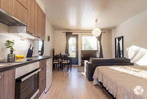 Cozinha moderna com armários de madeira, área de refeições com mesa e cadeiras, e um quarto com cama e uma janela grande.