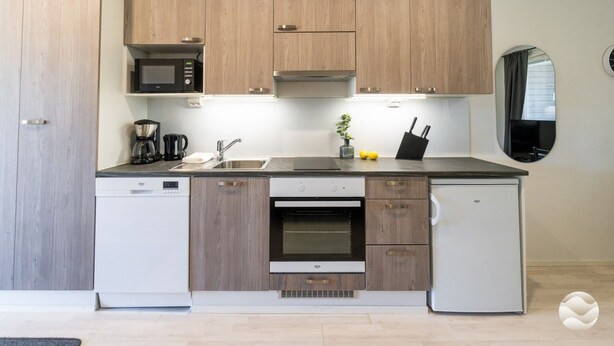 A modern kitchen with wooden cabinets, a microwave, a coffee maker, a sink, and a stove. - Meriheinä B7 by Holiday in Kalajoki (Kalajoki)