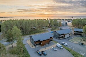 A modern building complex with multiple structures, a parking area, and a forested area in the background.