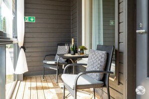 A balcony with wicker chairs, a table with a bottle and glasses, and a green emergency exit sign.