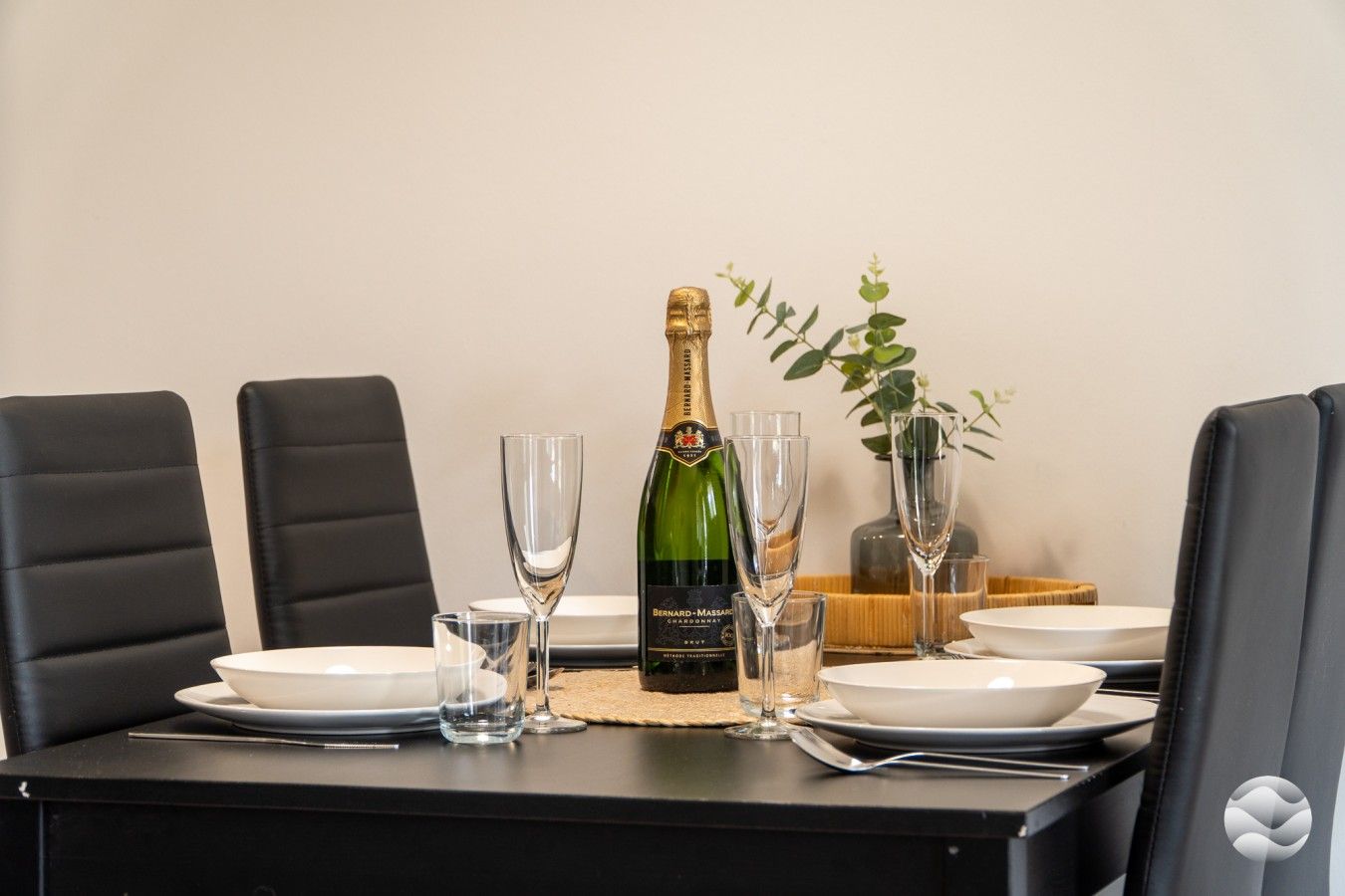 A dining table set with a bottle of champagne, four glasses, and plates.
