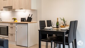 Cozinha compacta com eletrodomésticos modernos, área de jantar com mesa posta para dois e pequena geladeira.