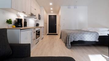 Una habitación funcional con kitchenette, cama y una pequeña zona de estar.
