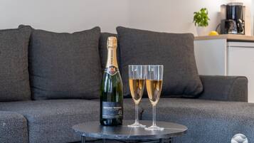 Bernard-Massard Chardonnay -pullo ja kaksi viinilasia pienellä pyöreällä pöydällä harmaan sohvan edessä.
