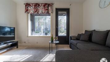 Sala de estar com televisão, sofá e janela com vista para árvores.