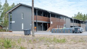 En moderne bygning med grå facade, en træterrasse og en carport med overdækket parkering.