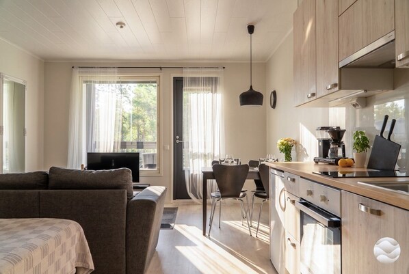 A modern kitchen with wooden cabinets, a dining area with a table and chairs, and a sofa in the living area.