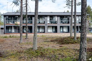 A modern two-story building with large windows and a flat roof, surrounded by trees.