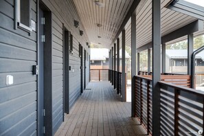 Un couloir couvert doté d’un plancher en bois, de rampes en métal et offrant une vue sur des bâtiments situés au loin.