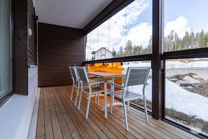 A wooden deck with a table and chairs, large windows, and a view of a snowy landscape. - Polar Charm G Holiday in Lapland (Ylläs)