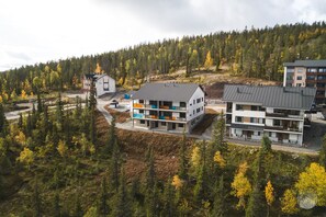 A modern multi-story building with a flat roof, surrounded by a forested area. - Polar Charm G Holiday in Lapland (Ylläs)