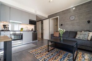 A modern kitchen with built-in appliances, a dining area with a coffee machine, and a living room with a sofa and a clock on the wall. - Polar Charm G Holiday in Lapland (Ylläs)